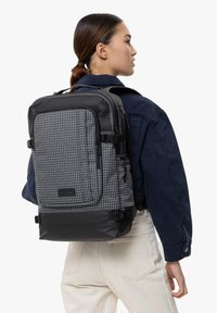 Zaino a scacchi nero e grigio realizzato in tessuto resistente, con molteplici scomparti con zip, spallacci imbottiti e base nera a contrasto.
