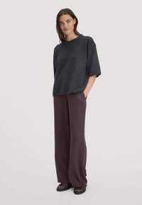 Felpa oversized grigia scura con maniche corte, abbinata a pantaloni larghi marrone scuro e calzature nere. Design semplice e minimale.