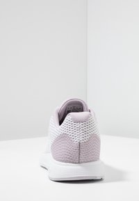 Chaussure de sport blanche avec une tige en mesh, des accents texturés violet clair et un col rembourré. Semelle en caoutchouc avec une surface antidérapante à motif.