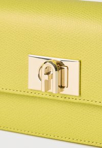 Κοντινή λήψη κλειδώματος με χρυσό κούμπωμα σε υφασμάτινη φάσα δερμάτινης τσάντας σε αποχρώσεις λάιμ πράσινου, με ορατές ραφές.