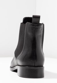 Czarny skórzany botek za kostkę z elastycznymi panelami po bokach, zaokrąglonym noskiem i niskim, warstwowym obcasem. Posiada pętelkę z tyłu ułatwiającą zakładanie.