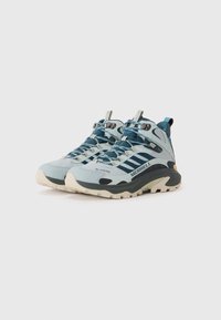 Para szarych i niebieskich butów trekkingowych Merrell z grubymi beżowymi podeszwami, z materiału Gore-Tex i sznurowanym zapięciem na białym tle.