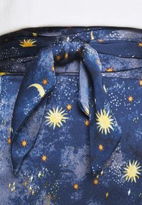 Marineblauer Stoff mit himmlischem Muster, das gelbe Sonnen und Monde zeigt, gebunden mit einer geknoteten Schleife. Weiche Textur mit leicht glänzender Oberfläche.