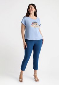 Jasnoniebieski t-shirt z krótkim rękawem z graficznym wzorem i napisem, w połączeniu z dopasowanymi niebieskimi spodniami i sandałami na cienkich paskach w jasnym kolorze.