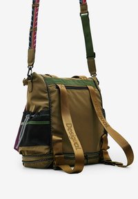 Brązowa nylonowa torba z zielonymi akcentami, wyposażona w siatkową boczną kieszeń, zapinane na zamek przegrody i kolorowy, wzorzysty pasek na ramię.
