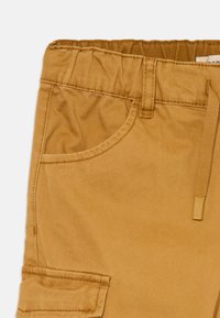 Pantalons couleur sable avec taille élastique, poche avant, cordon de serrage et poche à rabat sur le côté.