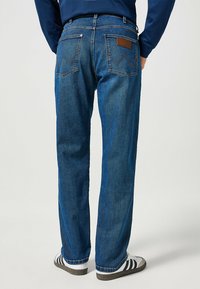 Granatowe dżinsy o prostym kroju, z wyszywanymi tylnymi kieszeniami w wzór zygzaka oraz brązową skórzaną naszywką z logo.