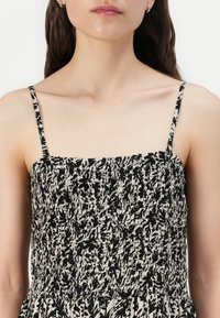 Femme portant une robe noire et blanche à motif floral sans manches avec de fines bretelles, montrant le décolleté et les épaules.