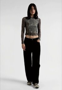 Top ajustado de mangas longas em tecido escuro e estampado; combinado com calças largas de veludo cotelê pretas e ténis pretos. O modelo está a fazer uma pose contra um fundo simples.