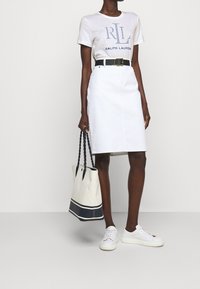 Vit denimkjol, kortärmad beige t-shirt med marinblå tryck, svart bälte, vita sneakers och en stor beige tote-väska med marinblå ränder.