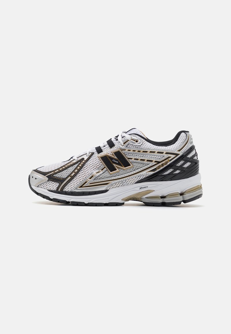 Baskets de sport blanches et noires avec tige en mesh, lacets, semelle rembourrée et accents dorés, vues de profil sur un fond uni.