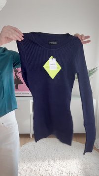 Top de manga longa em azul-marinho com decote redondo. O tecido é elástico com um acabamento texturizado. A etiqueta anexada é de cor verde brilhante.