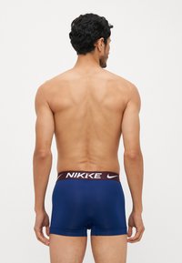 Mornarski plavi bokserice s ugrijanim elastičnim pojasom u bordo boji, na kojem je bijeli logo 'NIKE'. Glatka tekstura, prilagođen dizajn i minimalna pokrivenost.