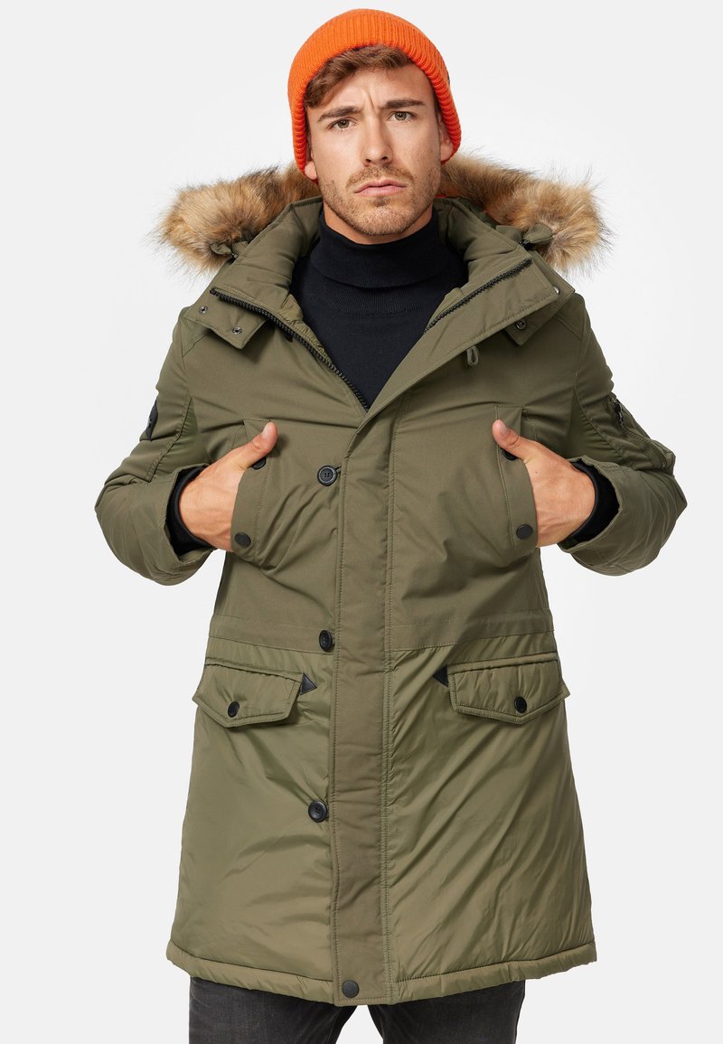 Parka verde oliva con capucha forrada de piel, cierres de botón y múltiples bolsillos. Presenta un exterior elegante y texturizado con un corte relajado.