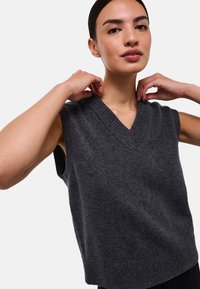 Pull en tricot sans manches gris foncé avec un décolleté en V et des bords côtelés. Texture douce et coupe décontractée, avec de grandes emmanchures pour le confort.