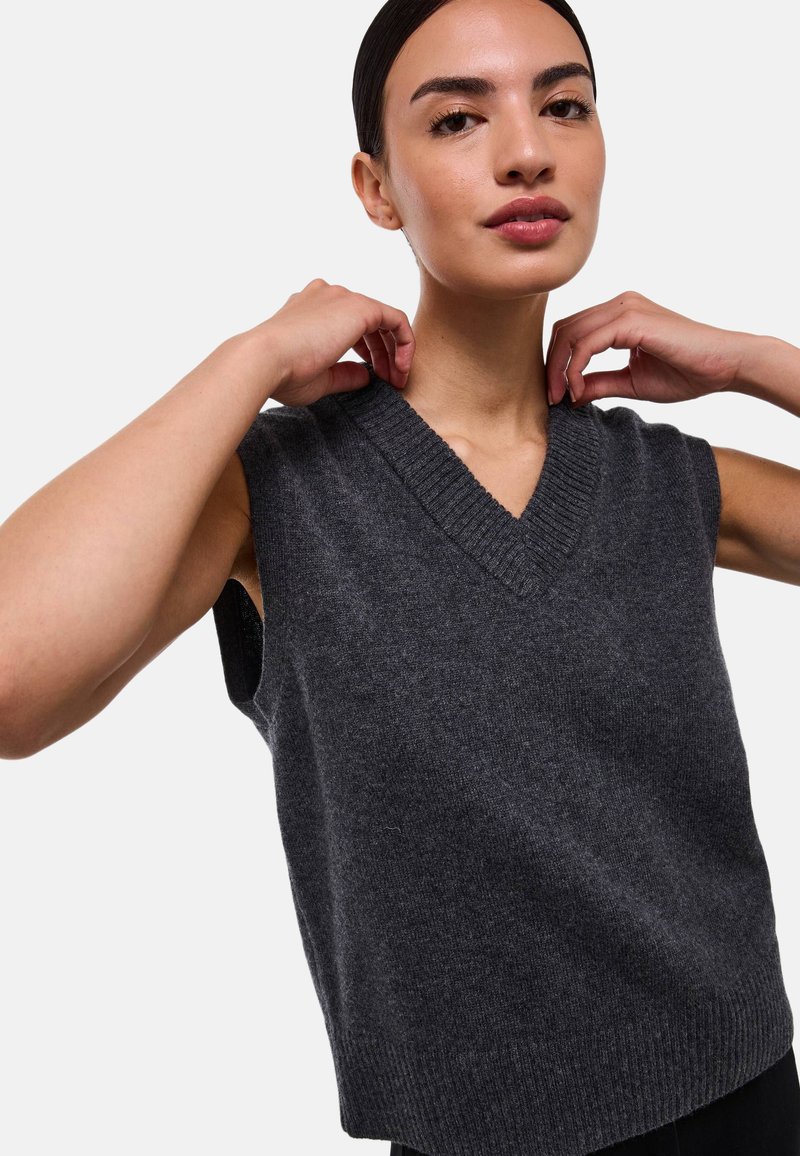 Pull en tricot sans manches gris foncé avec un décolleté en V et des bords côtelés. Texture douce et coupe décontractée, avec de grandes emmanchures pour le confort.