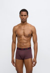 Maroon boxer briefs with a black elastic waistband featuring red "HUGO" branding. Smooth, stretchy fabric with a fitted design.