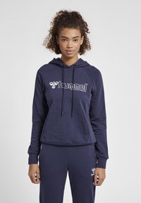 Marinblå hoodie med dragsnoddar, framficka och vit "hummel" logotyp. Tyget verkar mjukt med en slät yta, kombinerat med matchande joggers.