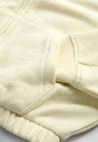 Close-up van een crèmekleurige sweatshirtmouw met geribbelde gebreide pols en details van voorzakstiksels.