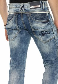 Verblasste blaue Denim-Jeans mit dekorativen Nähten, gerippten Akzenten auf den Gesäßtaschen und einem Markenlabel über dem Bund.