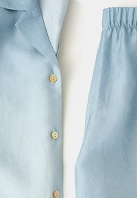 Lekki niebieski żakiet z pofałdowanego materiału z trzema kremowymi guzikami oraz pasujące spodnie z elastyczną talią na białym tle.