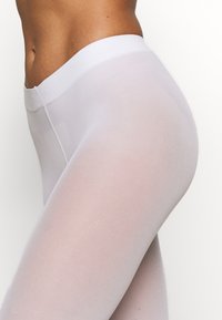 Leichte, transparente weiße Leggings mit glatter Textur, ausgestattet mit einem breiten elastischen Bund und einer figurbetonten Passform.