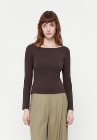 Top pe lungi, ajustat, din material elastic de culoare maro închis, cu un decolteu larg și detalii subtile de broderie la talie. Asortat cu pantaloni bej deschis.