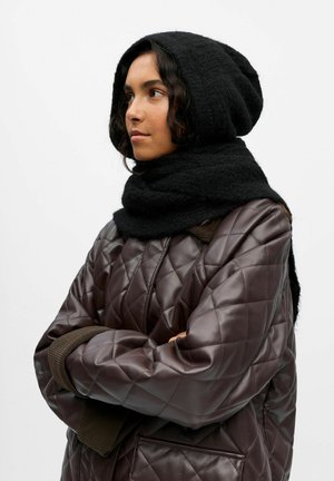 Melnā adīta kapuce un šalle, apvienota ar Quilted brūnu ādas jaku, kurai ir dimanta raksts un ribināti piedurknes.