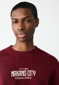 Ma�ślany sweatshirt z prążkowanym dekoltem okrągłym, z białym napisem "TOKIO" i "NAKANO CITY RENGA ZAKA" na przodzie.
