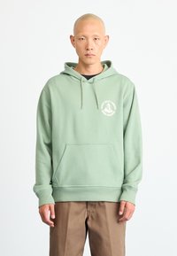 Hoodie verde claro feito de mistura de algodão, com um bolso frontal, capuz com cordão e um logótipo circular no peito. Ajuste descontraído.