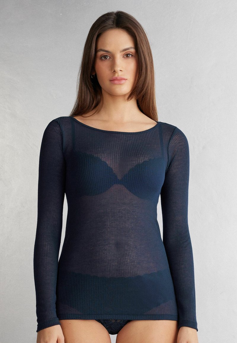 Granatowa bluzka z długim rękawem o przezroczystej prążkowanej teksturze, z okrągłym dekoltem i dopasowanym krojem. Nałożona na czarny element dolny.
