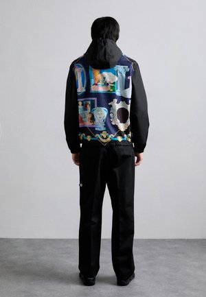 Black jacket with a patterned back featuring classical art visuals. Hooded design, lightweight fabric, paired with black pants and shoes.