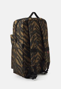 Zaino a strisce tigre marrone e nero con maniglia superiore, chiusura con zip e spallacci imbottiti. Include una tasca laterale e tessuto testurizzato.