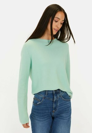 Mintgroene, geribbelde gebreide trui met een ronde halslijn en lange mouwen, gecombineerd met blauwe spijkerbroek. De trui heeft een ontspannen pasvorm.
