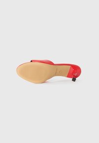 Red patent leather high-heeled shoe with an open toe and tan rubber outsole featuring a horizontal ribbed pattern. Black accent at the heel.