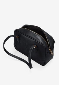 Bolso de mano de piel negra con cierre de cremallera, detalle de logo en relieve, forma redondeada, dos asas cortas y acentos de metal dorado.