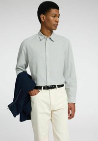 Lichtgrijs long sleeve shirt met een kraag, knoopsluiting en gestructureerde stof. Gecombineerd met crèmekleurige broek en een marineblauwe jacket.