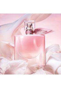 Rosa glass parfymeflaske med rund form, toppet med et klart, firkantet lokk og dekorert med et glitrende rosa bånd, plassert mot myke stoffer.