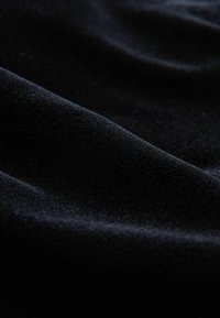 Schwarzer Samtstoff mit glatter Textur und weichem Glanz, der subtile Wellen und Falten zeigt und die reiche, tiefe Farbe betont.