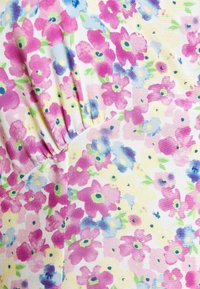 Tissu floral avec des fleurs roses, bleues et jaunes sur un fond blanc. Présente une section texturée et froncée, créant un effet superposé.