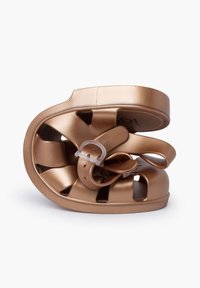 Bronze slip-on shoe made of flexible material, featuring cut-out patterns and a buckle strap, displayed in a twisted, compact form.