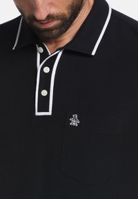 Zwarte polo met contrasterende witte kraag en knopenlijst. Bevat drie knopen en een klein pinguïnlogo op de borstzak.