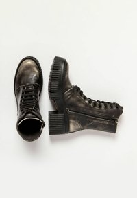 Bottines noires à lacets avec semelles épaisses et zips sur le côté, une botte debout et l'autre couchée sur le côté sur un fond blanc.