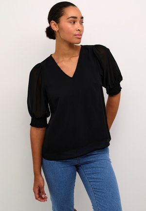 Sort bluse med V-hals, puffede gennemsigtige ærmer og smockede manchetter. Stoffet virker let og har en glat struktur, parret med blå jeans.