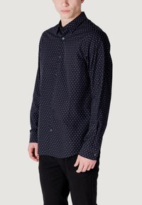 Camicia a maniche lunghe con bottoni di color navy con un motivo di punti bianchi sparsi. Presenta un colletto classico e polsini con bottoni, realizzata in un tessuto leggero.