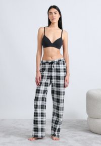 Μαύρο μπουστάκι συνδυασμένο με άνετο, ασπρόμαυρο καρό παντελόνι πυτζάμας με κορδόνι στη μέση. Το ύφασμα φαίνεται μαλακό με χαλαρή εφαρμογή και φαρδιές πιέτες.