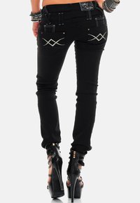 Schwarze Skinny-Jeans mit dekorativen Diamantnähten auf den Taschen, versehen mit Metallakzenten. Kombiniert mit schwarzen Sandalen mit hohen Absätzen und Riemchen.