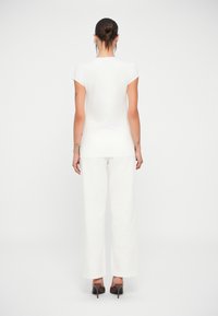 Un haut en coton blanc avec des manches courtes, associé à un pantalon large blanc, vu de l'arrière. Texture lisse ; design simple.