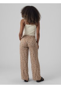 Brązowe, wzorzyste spodnie o szerokich nogawkach z wysokim stanem i gładkiego, lekkiego materiału, zestawione z jasnym topem na ramiączkach.