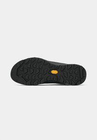 Black rubber outsole with deep tread pattern, featuring a central logo. Durable design for traction on various surfaces.